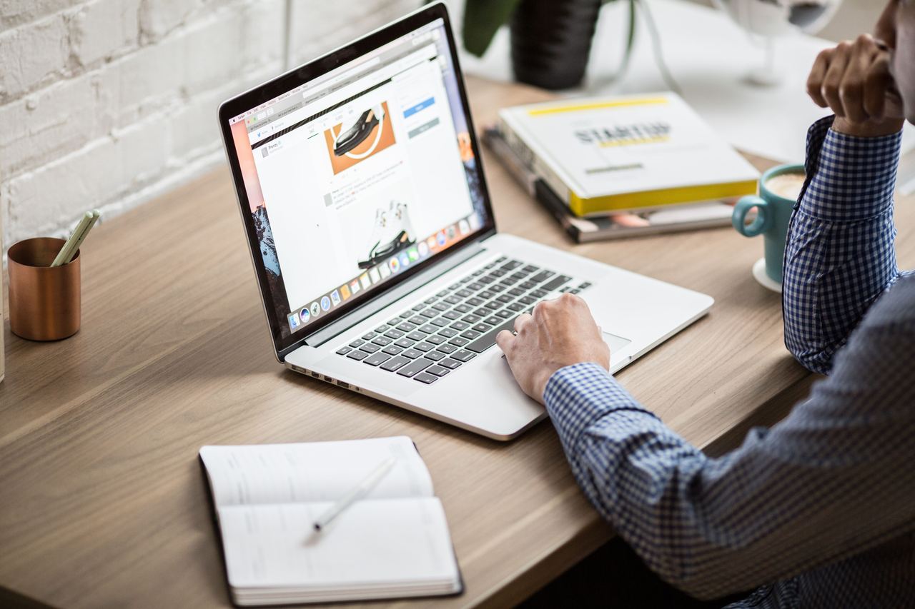 Seller at a warm wood desk reviewing an ecommerce catalog on a laptop